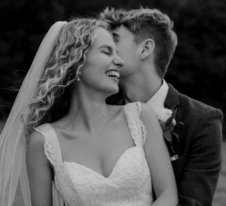 Black & white image of bride and groom as groom wraps his arms around bride on their wedding day