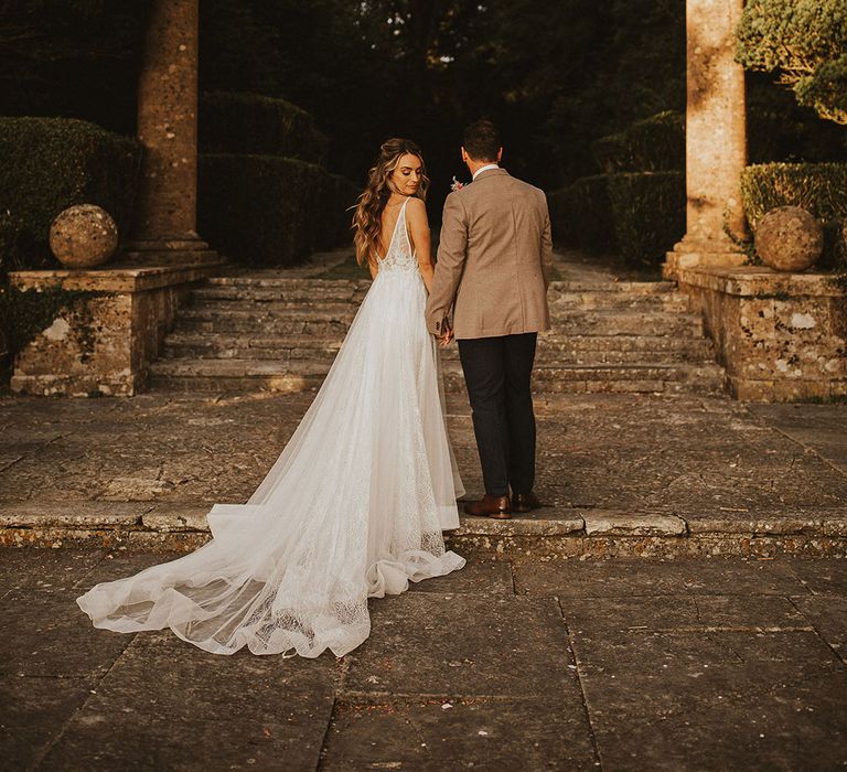 Bride & groom stand on grand staircase outdoors as the sun shines around them