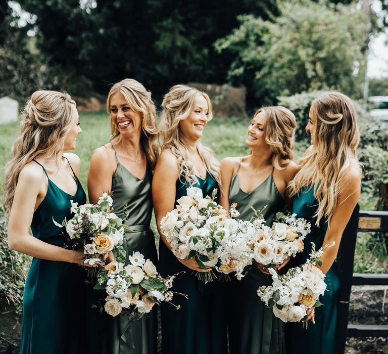 Bridesmaids in mixed green satin bridesmaid dresses from Rewritten Bridesmaids hold white and green wedding bouquets at church wedding