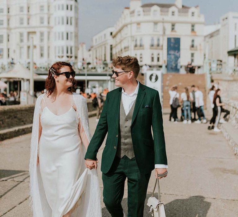 Bride & groom walk hand in hand on their wedding day through Brighton as they both wearing sunglasses on their wedding day