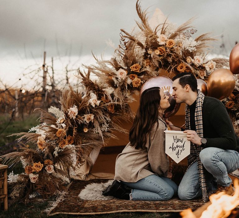 Boho bell tent wedding proposal with dried and fresh flowers, metallic balloons and "how 'bout it banner"