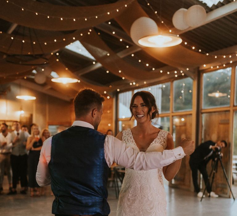 Bride in v neck lace wedding dress has first dance with groom in white shirt and waistcoat during rustic barn wedding reception