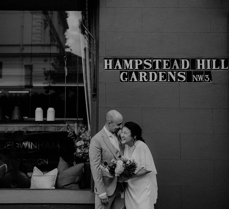 Bride & groom stand outdoors as they lovingly embrace on their wedding day in black & white image 