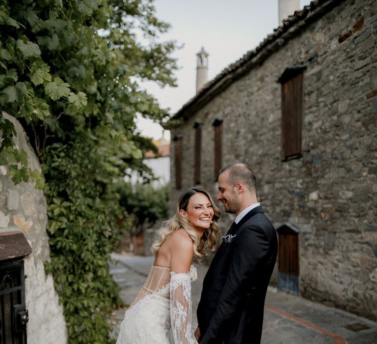 Bride & groom hold hands and look lovingly at one another on their wedding day as they walk through the streets of Greece 