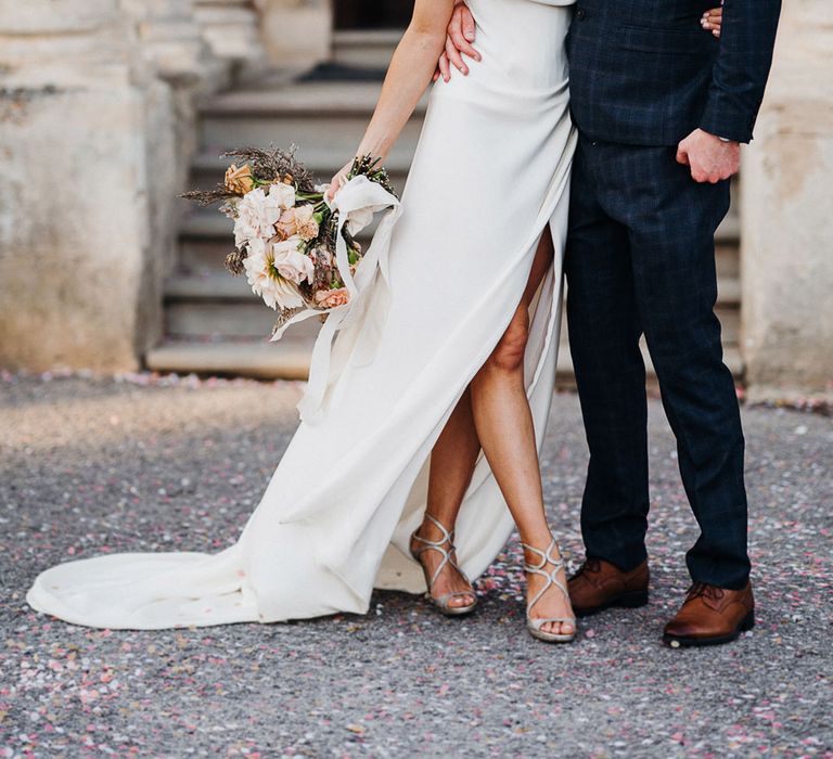 Groom in blue checkered suit and bride in off the shoulder front slit wedding dress and silver heels share a kiss