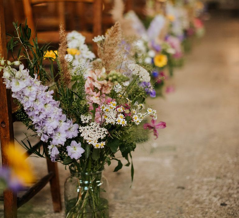 Pretty and colourful flowers in glass vases as aisle wedding decor 