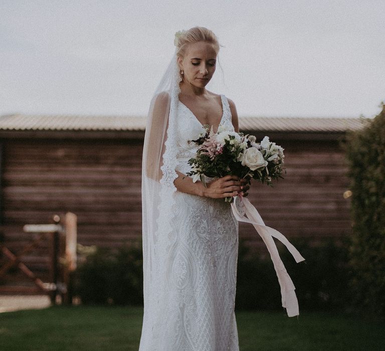 Bride in lace v-neck wedding dress and lace veil with pink and white wedding bouquet tied with pink ribbon 