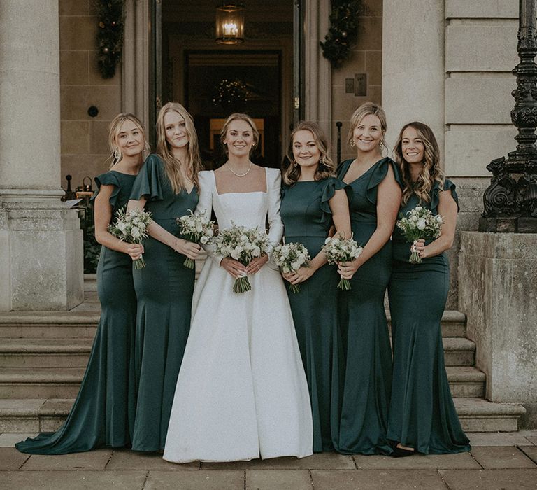 Bridal squad wearing Suzanne Neville, long white wedding dress and long bottle green dresses with white mixed floral bouquets