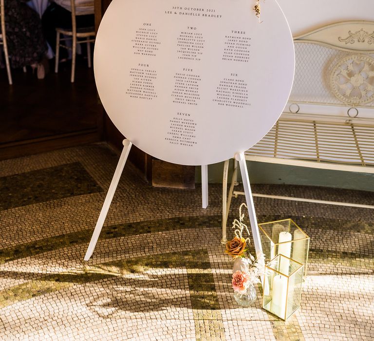 Circular wedding seating chart sign topped with autumnal flowers and gold rimmed vases with candles