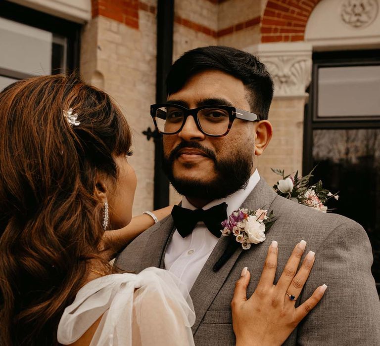 Bride showing off wedding ring with groom in grey suit, black bow tie and mixed neutral boutonniere 