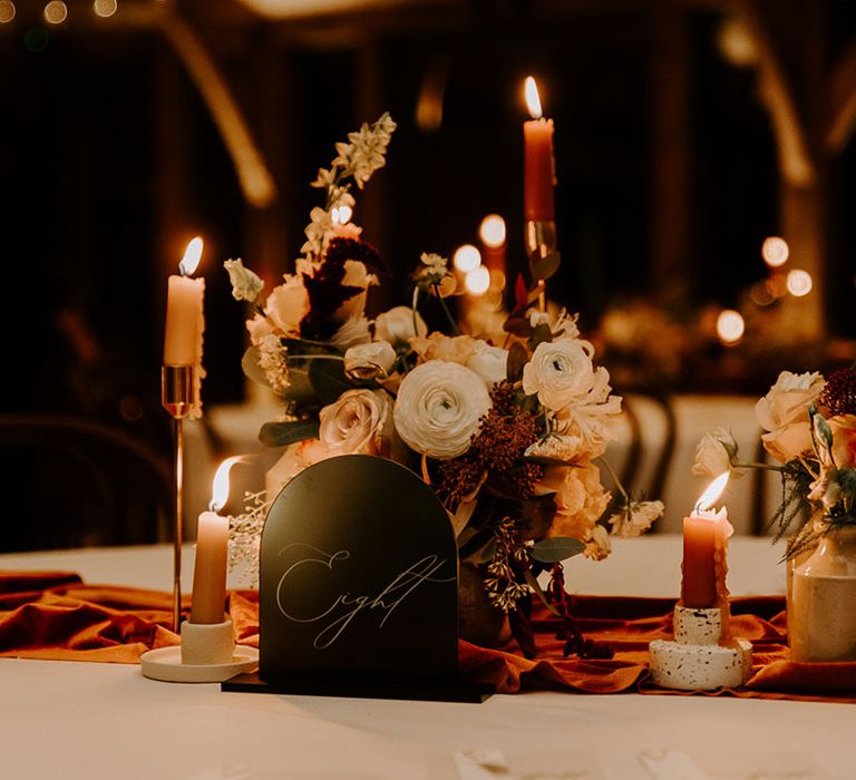 Orange table runner with orange candles and autumnal flower arrangement with black table sign 