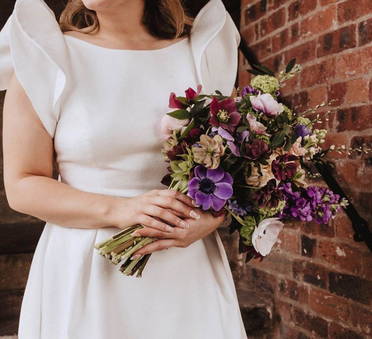 Bride with white pattern abstract nails with white headband, red lipstick and Jesus Peiro wedding dress holding purple and burgundy wedding bouquet 