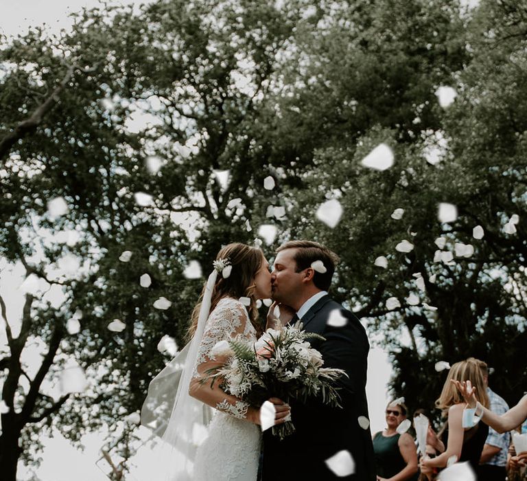 Bride and groom kiss as white confetti is thrown over the couple in celebration 