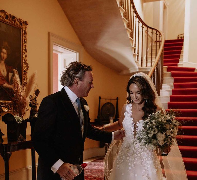 Father of the bride meets the bride at the bottom of the steps to take her to the outdoor wedding ceremony