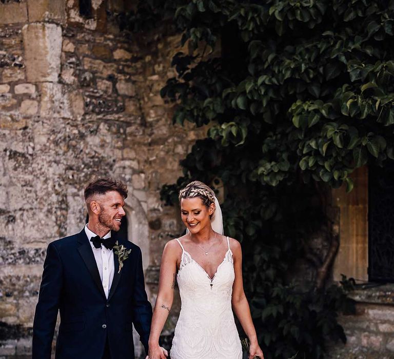 Bride and groom walk with their hands intertwined for their summer outdoor wedding 