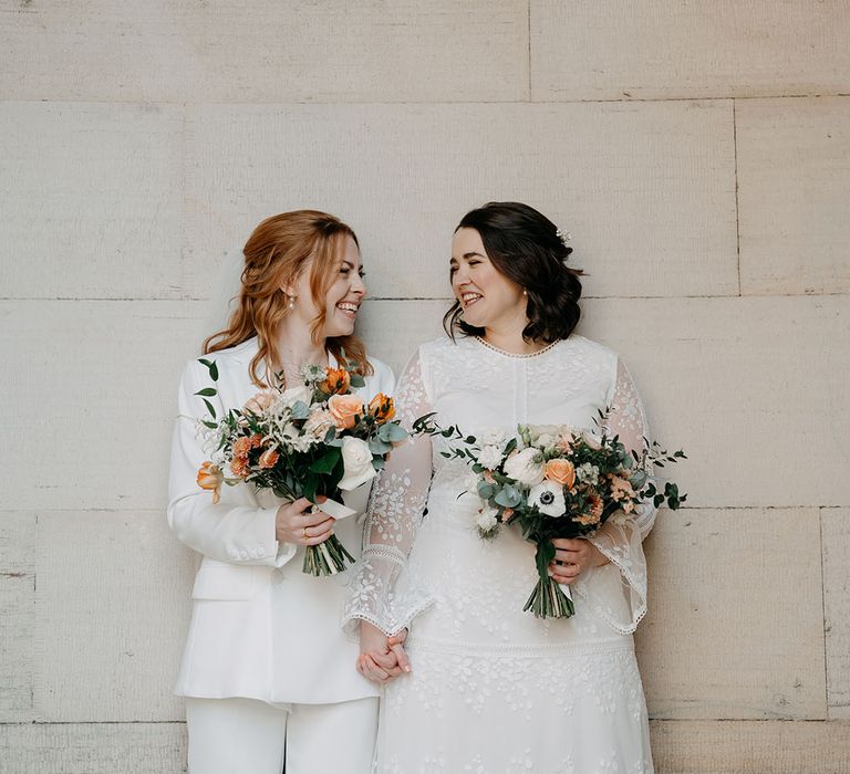 Brides stand together holding bright floral bouquets for intimate and relaxed wedding day