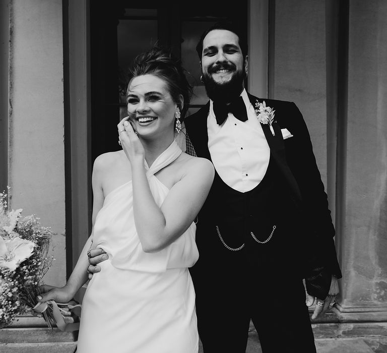 Groom in a horseshoe waistcoat with bow tie and chain with his bride in a satin halter neck wedding dress