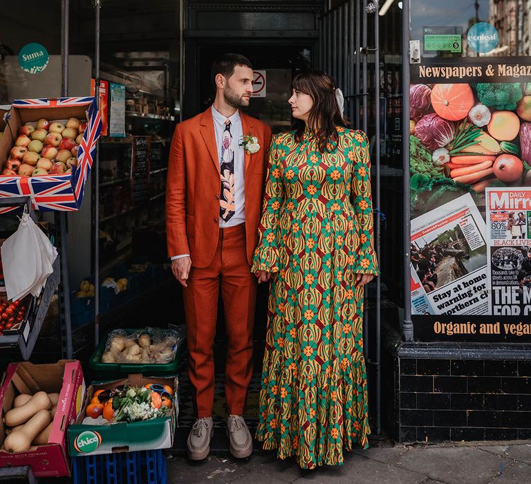 Bride & groom hold hands outdoors as groom wears orange Paul Smith linen suit complete with floral tie 