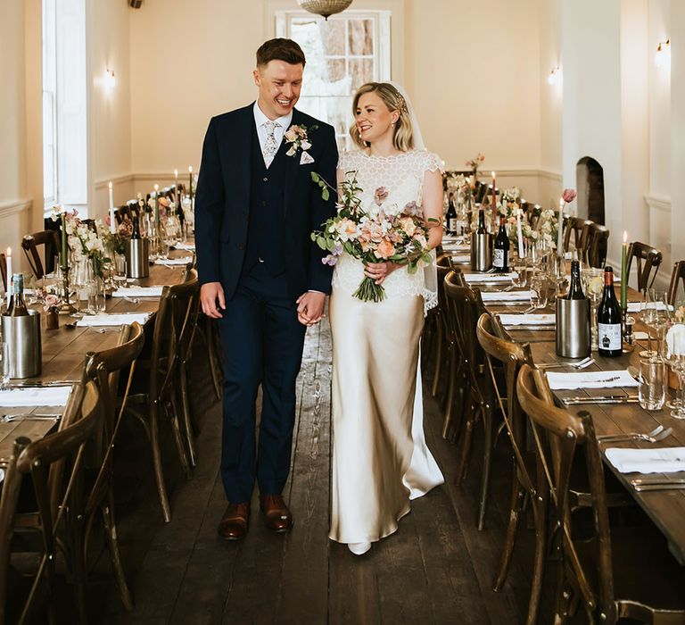 Bride & groom walk through wooden tables complete with pastel floral bouquets at Aswarby Rectory 