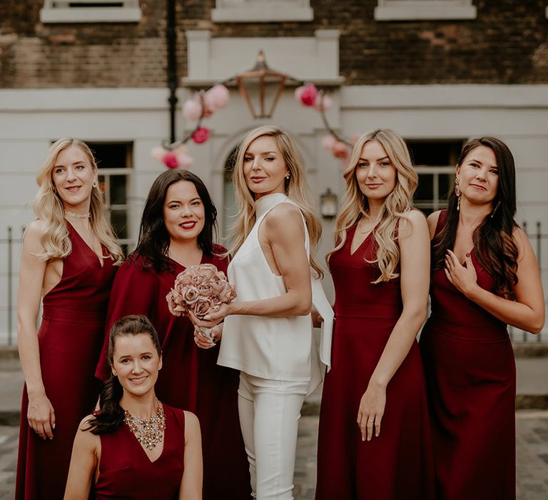 Bride in satin top and white trousers with the bridesmaids in their dark red dresses 