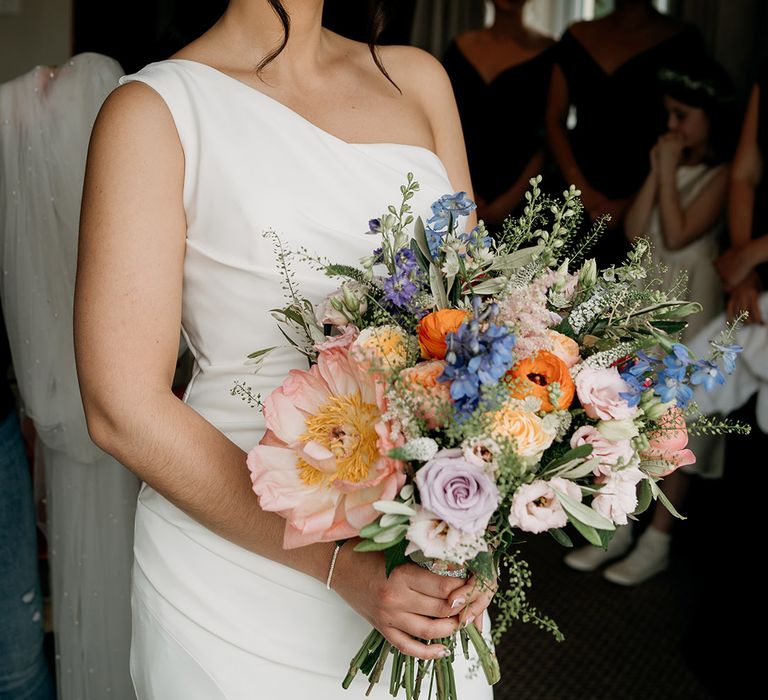 Bride holding pink, orange and blue wedding wildflower bouquet with one shoulder wedding dress with red lipstick 