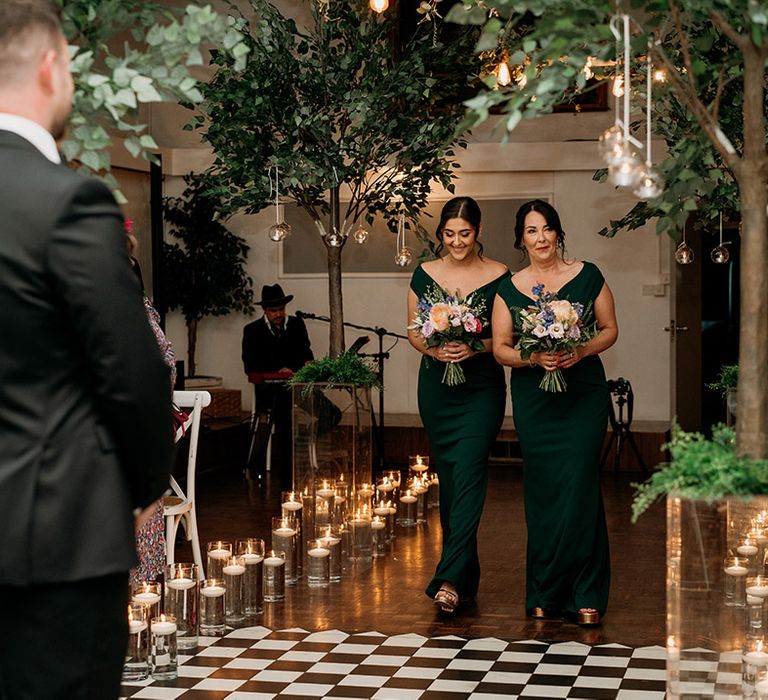 Bridesmaids in green bridesmaid dresses walk down the aisle together at Larkspur Lodge 