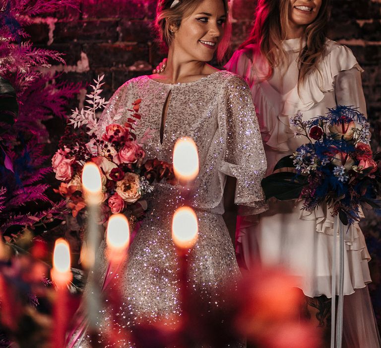 Two brides stand together under a neon pink 'Love Rocks' sign