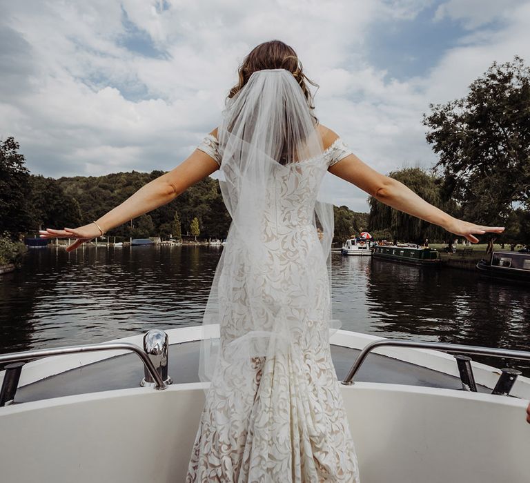 Bride in a boho lace wedding dress from Lovely Bride with a veil from Britten Weddings as she does the Titanic pose on the boat 