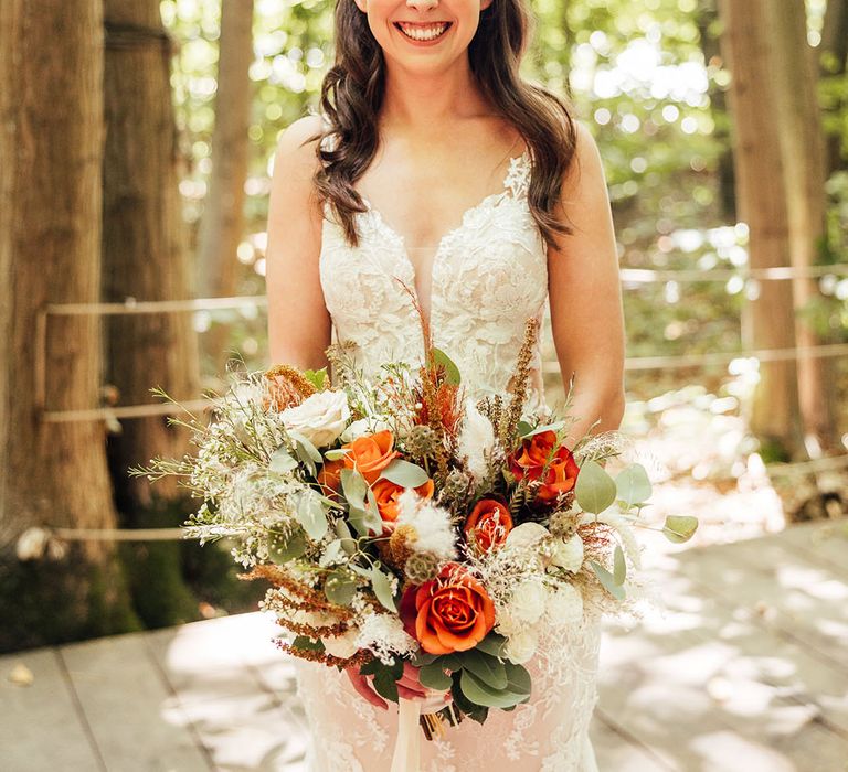 Bride with half up half down hair style in a lace wedding dress and white and orange rose wedding bouquet 