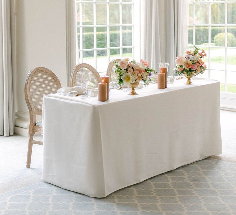 Small top table with a white tablecloth, pastel colourful wedding flower arrangements and neutral pillar candles 