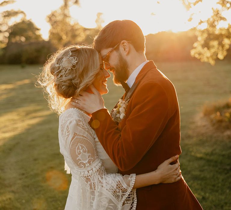 Golden hour shot of the bride in a boho lace wedding dress with the groom in an orange tuxedo sharing a kiss 