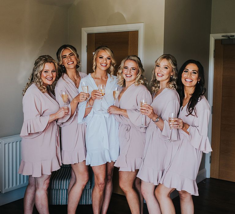 Bridesmaids in pink ruffle robes and matching fluffy slippers with the bride in a white robe