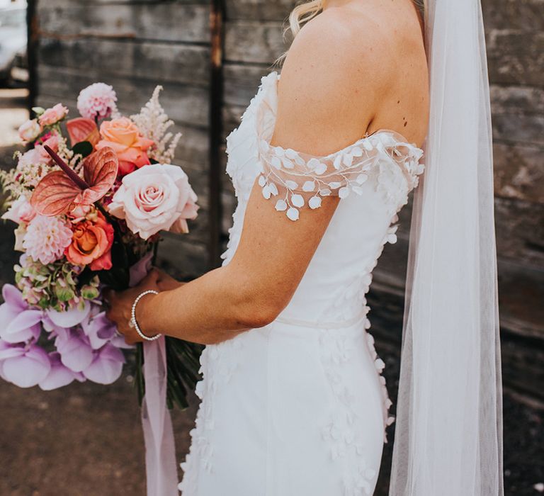 Bride holding a pink and purple wedding bouquet with bride in a leaf design off the shoulder wedding dress