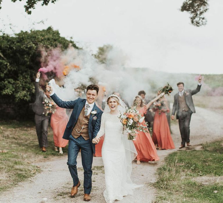 Bride and groom walk leading their wedding party with smoke bombs 