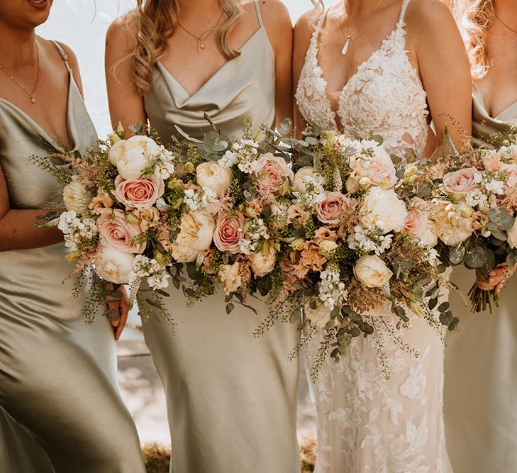 Bridesmaids in cowl neck satin bridesmaid dresses stand with bride in Essense Of Australia lace wedding dress holding pastel floral bouquets 