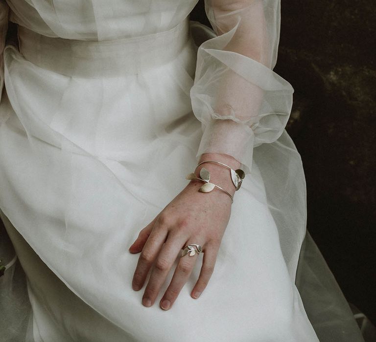 Bride wearing a gold leaf bridal necklace and matching cuff bracelet with a sheer long sleeve wedding dress