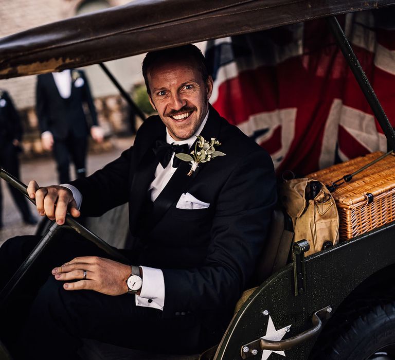 Groomsman in black tie driving the Jeep wedding transport with flag of Great Britain in the back 