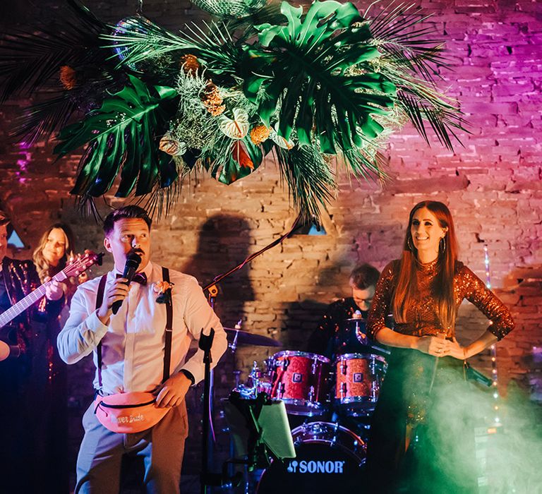 Wedding band performs for the evening with palm leaves, tropical flowers and bright lights 