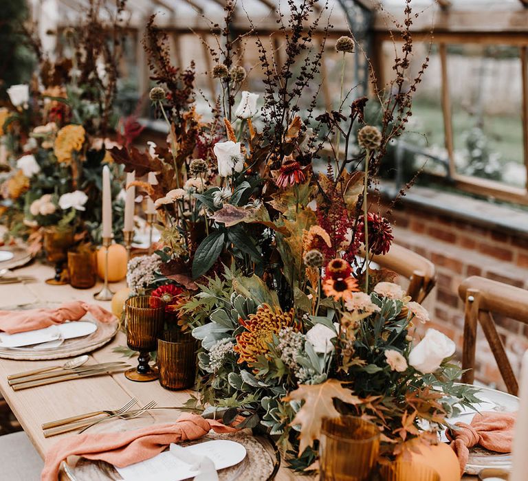 Glasshouse wedding venue with orange and red flower centrepiece, coloured glassware and pumpkin decor 