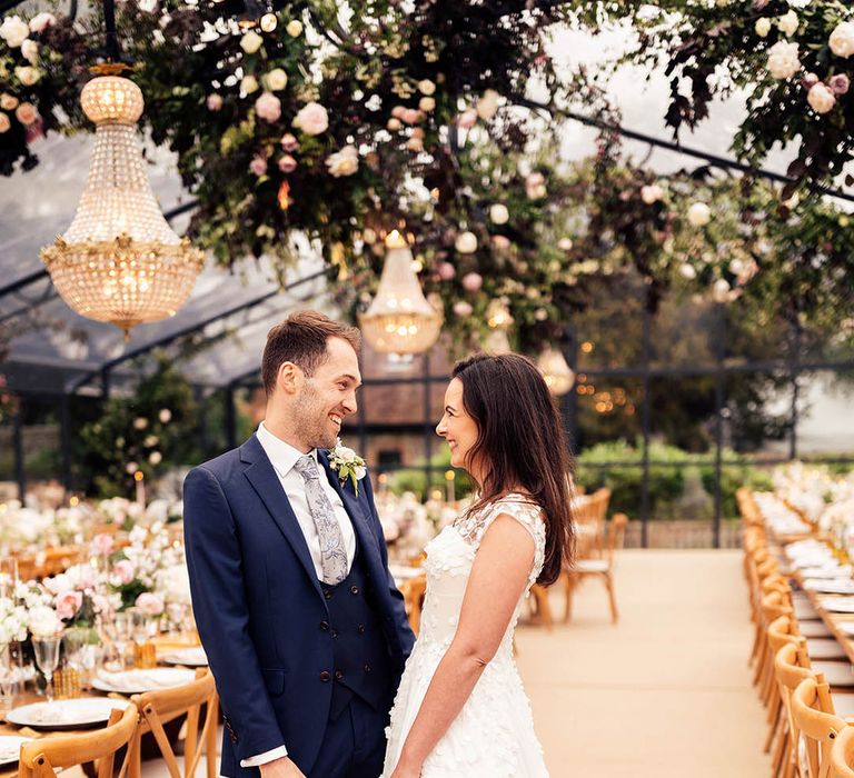 Bride in applique Phillipa Lepley wedding dress with the groom in blue three piece suit at their glass marquee reception 