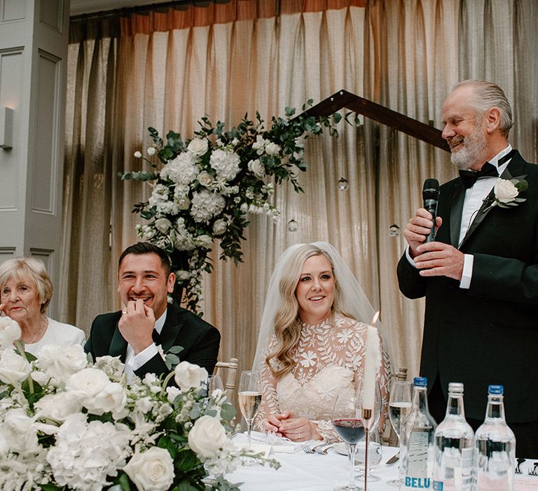 Bride & groom during wedding reception complete with classic white floral decor and hexagon arch