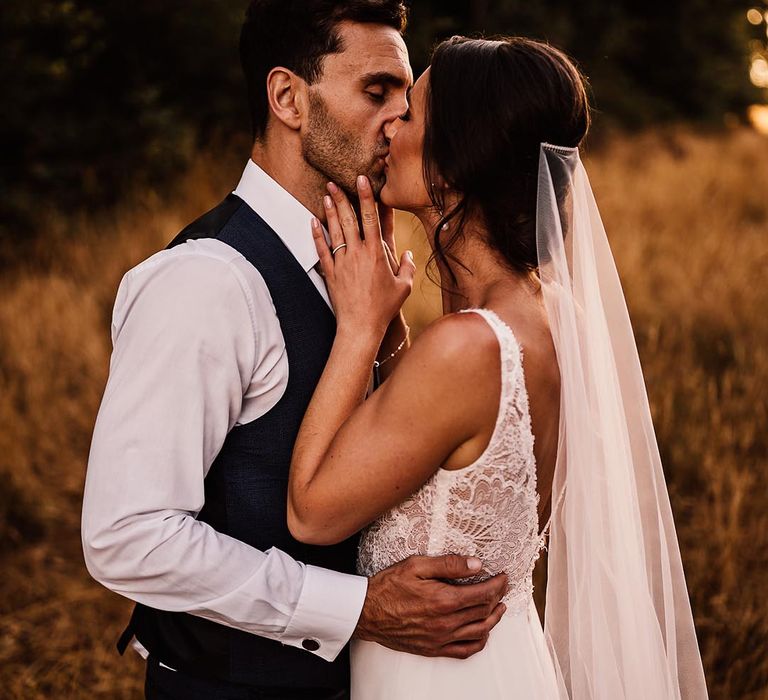 The bride touches the groom's face as she kisses him on their wedding day