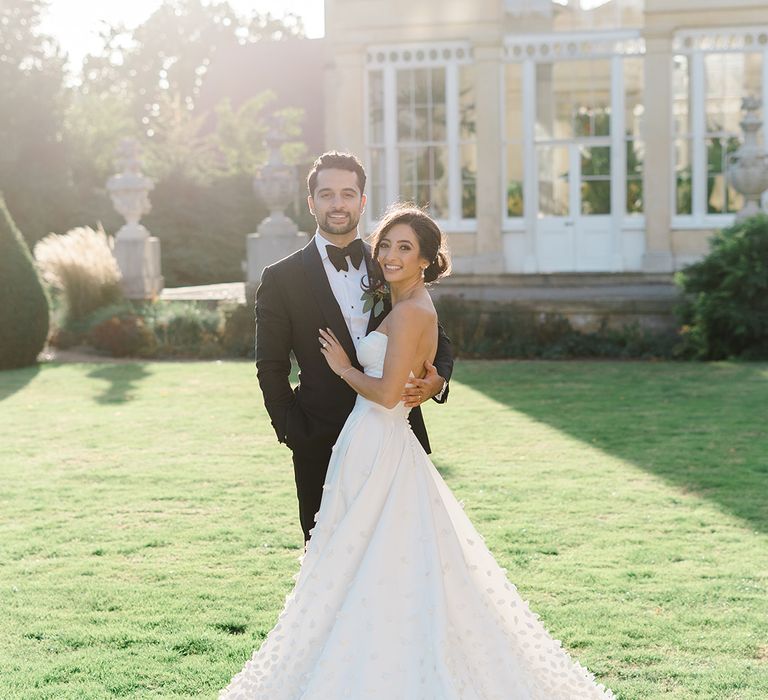 Bride wears Emma Beaumont bespoke wedding dress and stands with her groom in black-tie 