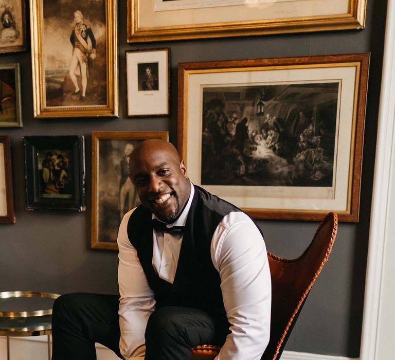 Groom in black waistcoat, suit trousers and black bowtie sitting on orange chair in Pepper Arden Hall 