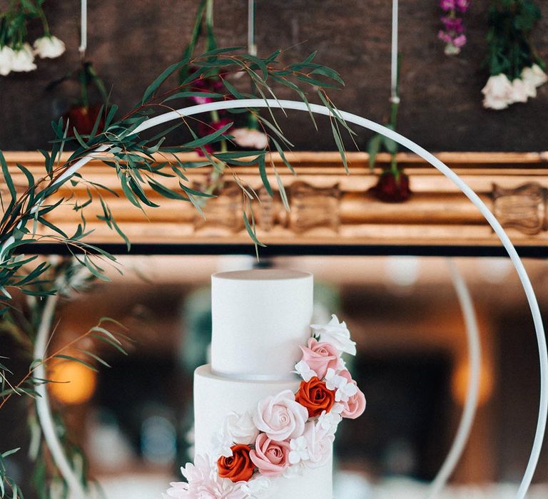 Three tier white iced wedding cake with pink and red iced flower decorations 