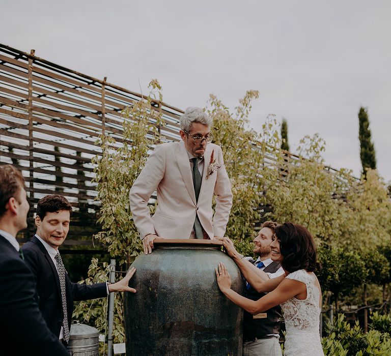 Groom gets inside a giant plant pot at Architectural Plants Venue with Bride and friends watching