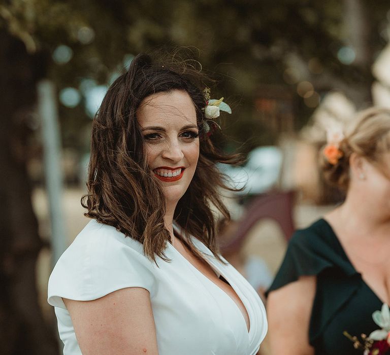 Smiling bride with short brown hair and red lipstick with flower hair accessory waiting for the bride for their lesbian wedding 