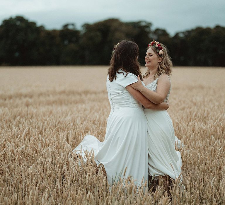 Bride in short sleeve wedding dress embracing bride with a sparkly wedding dress standing in a field together 