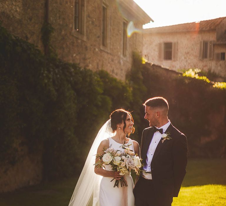 Bride in simple satin dress poses with Groom during golden hour wedding photography