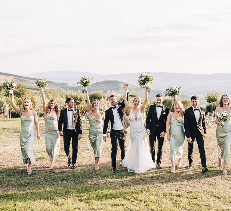 Bride & groom walk alongside their bridesmaids in pale green cowl neck dresses and groomsmen in black-tie